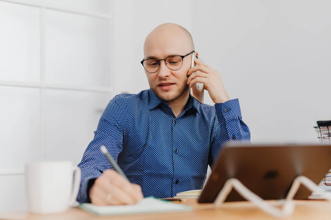 Mann am Schreibtisch telefoniert und macht sich Notizen