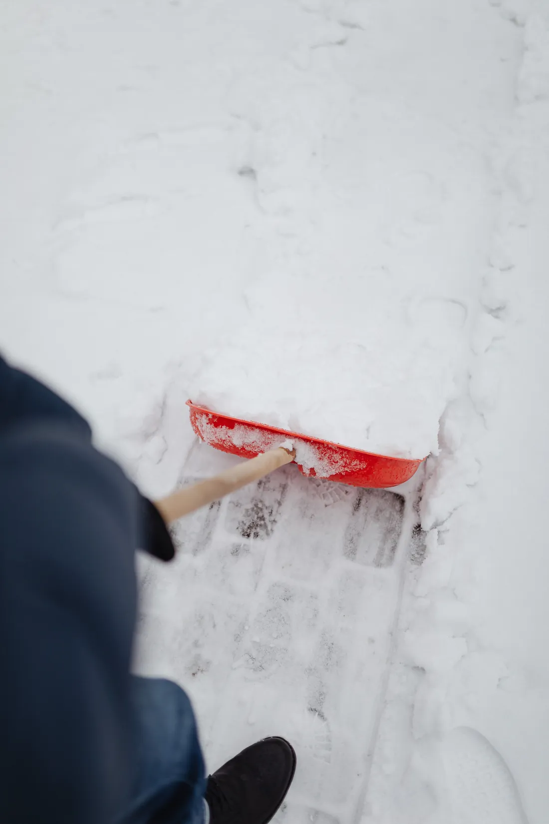 Person schippt Schnee von einem verschneiten Gehweg