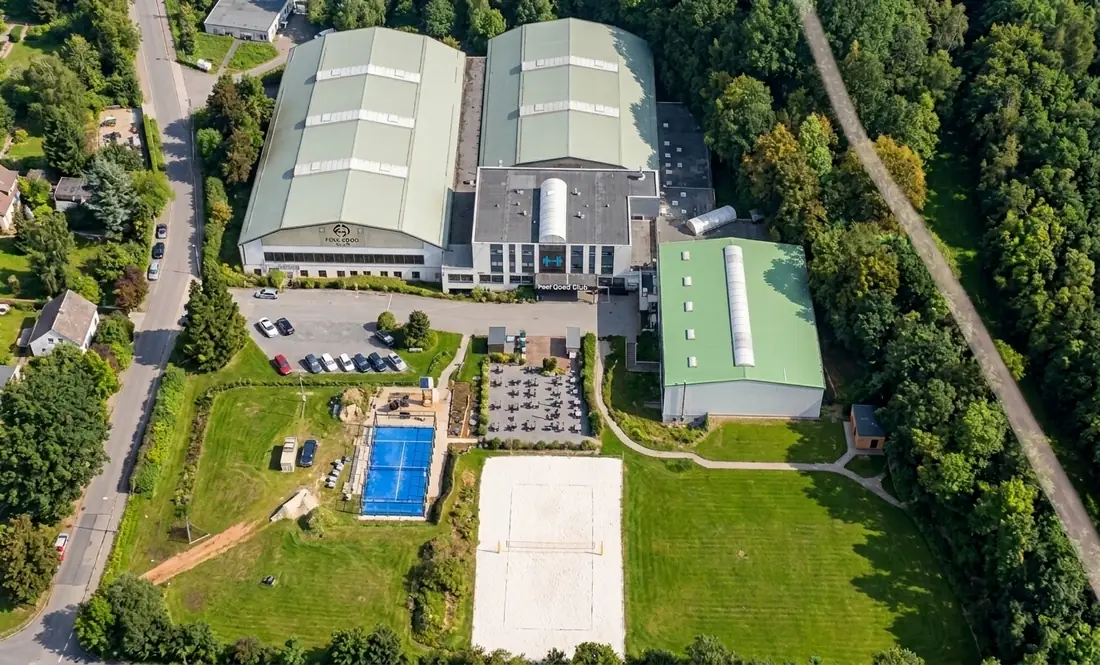 Luftaufnahme eines Betriebsgeländes mit Hallen, Pool und Beachvolleyballfeld