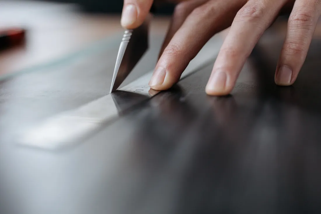 Nahaufnahme einer Hand, die mit einem Cuttermesser eine Glasscheibe anritzt